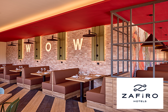 Bar mit braunen Tischen und St&uuml;hlen, an der Wand die Leuchtschrift WOW